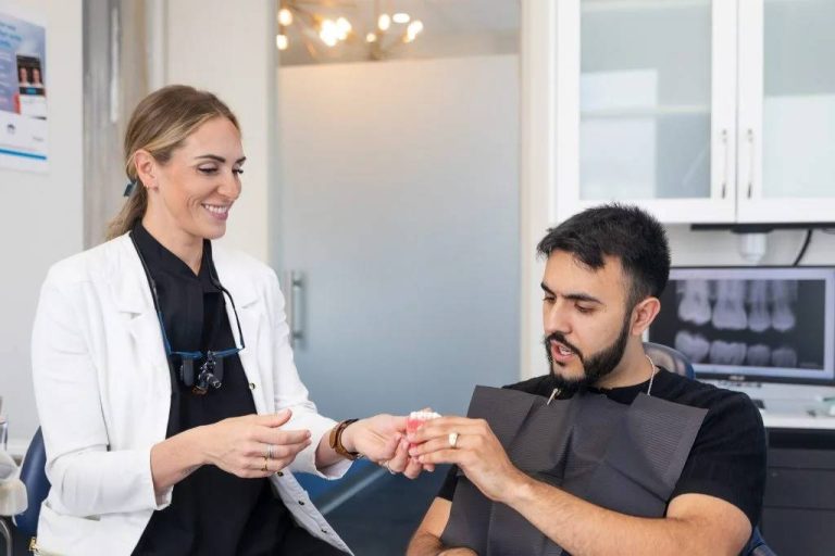 Female dentist in white coat smiles while consulting with male patient in bright modern dental clinic