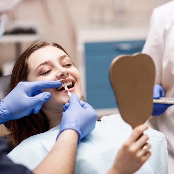 A woman examines her reflection in a mirror after undergoing cosmetic dental surgery. She smiles, admiring the improved appearance of her teeth